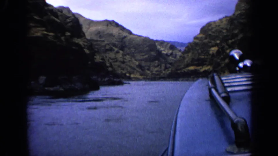 1963 Idaho 8mm frame showing a first-person boat view on calm river water between dark rocky hillsides.