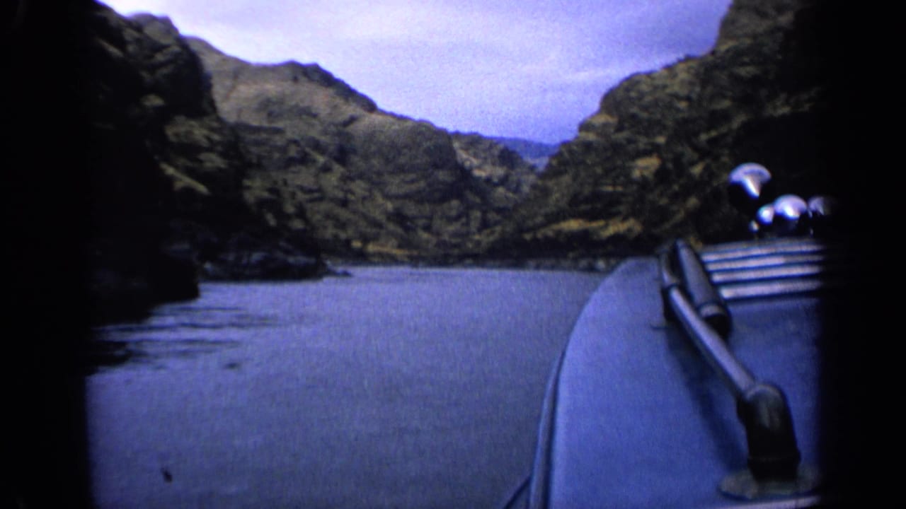 First-person 8mm view from a boat traveling through an Idaho river canyon, with railings visible at right.