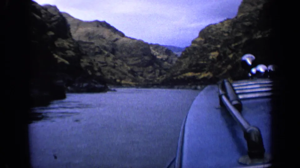 First-person 8mm view from a boat traveling through an Idaho river canyon, with railings visible at right.