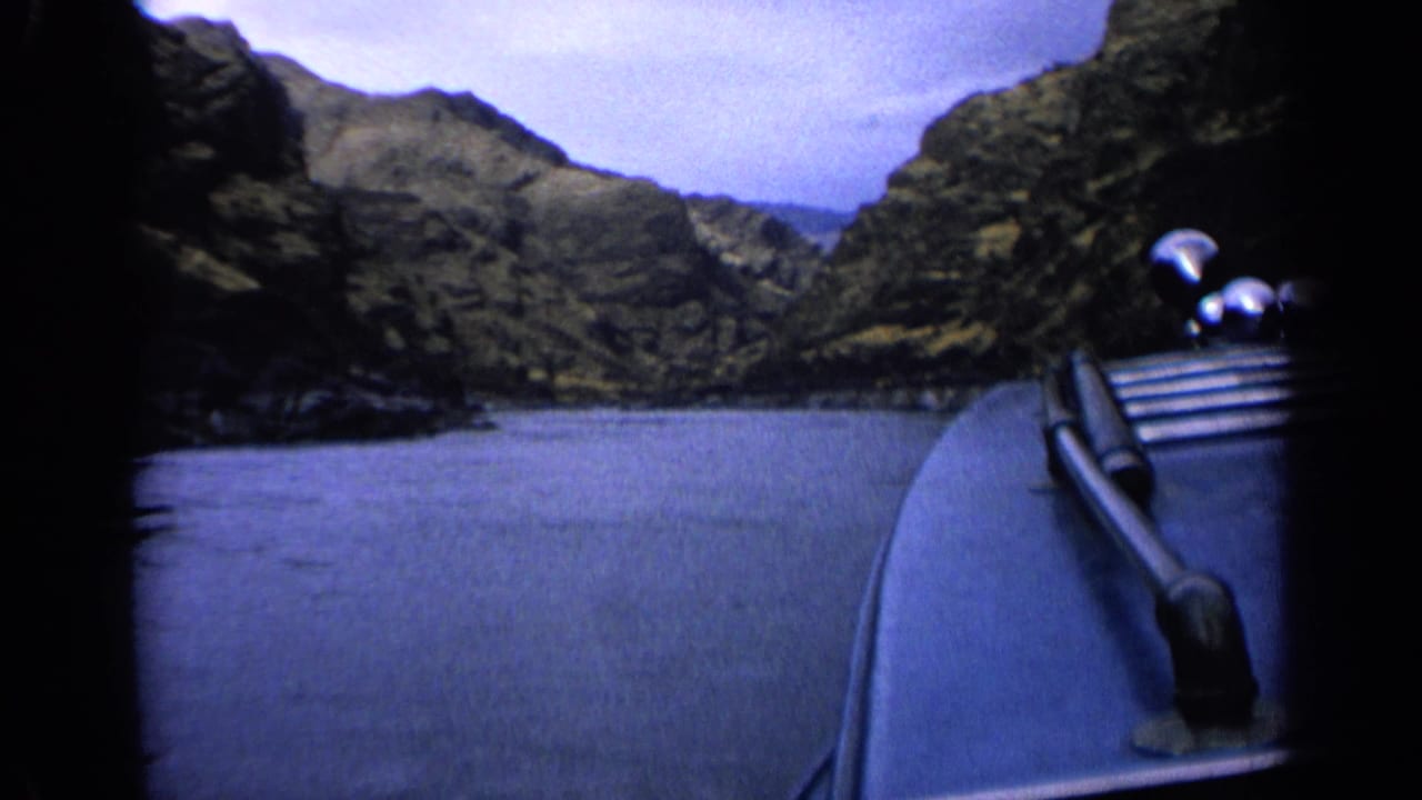 1963 Idaho home-movie frame from a moving boat, showing calm water and rugged canyon walls ahead.