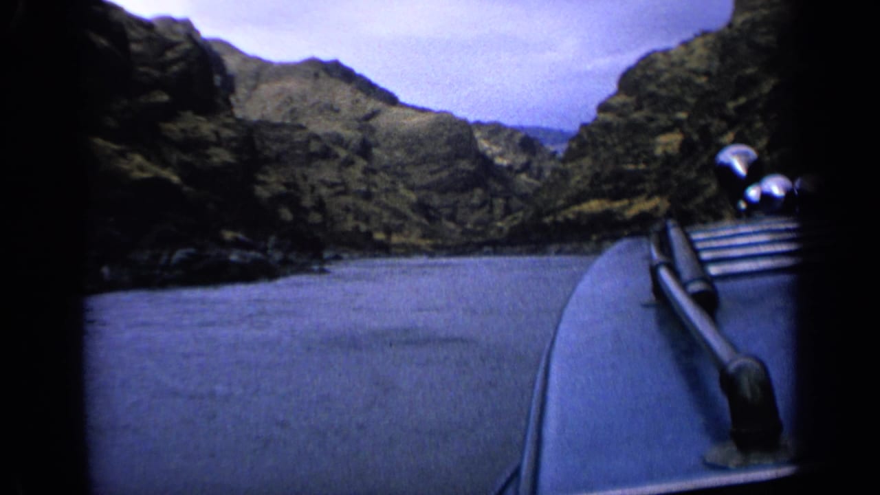 8mm Idaho river travel frame with the boat bow in the foreground and steep rocky hills beyond the water.