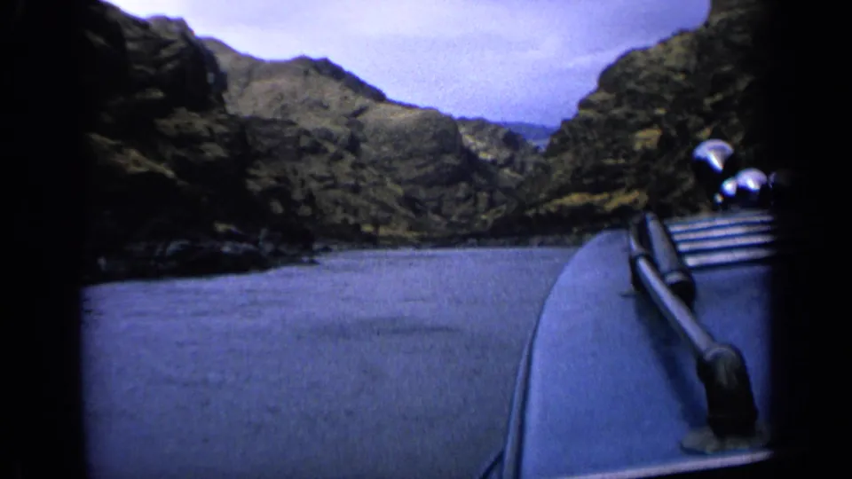 8mm Idaho river travel frame with the boat bow in the foreground and steep rocky hills beyond the water.