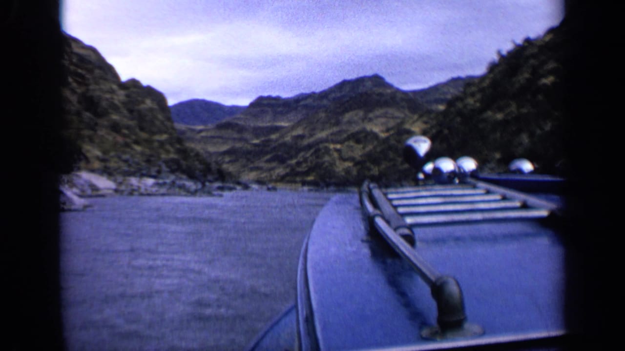 1963 Idaho home-movie view over a blue boat deck toward rocky hills and calm canyon water.