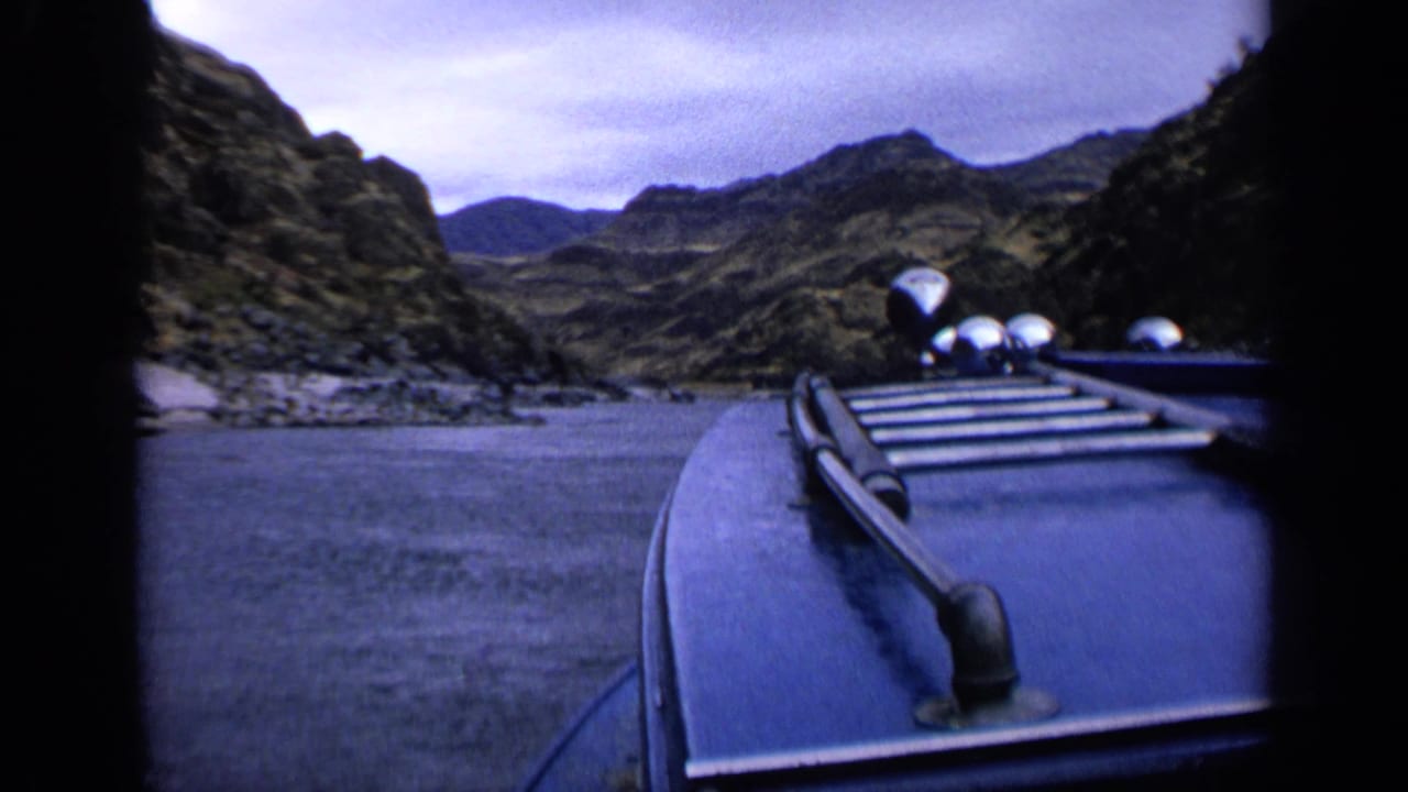 1963 Idaho home-movie frame with boat hardware in the foreground and rugged canyon slopes ahead.