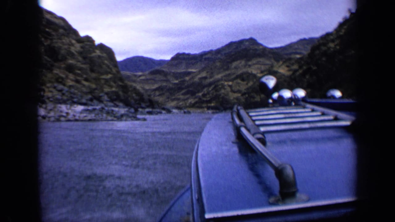 Boat bow and railing moving through a rocky river canyon under cloudy sky.