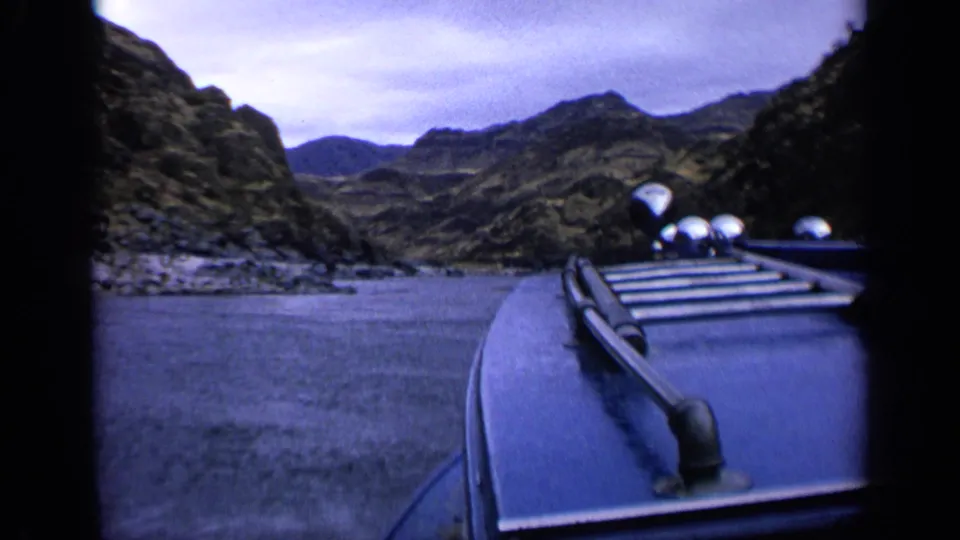 1963 Idaho 8mm frame showing a blue boat deck and railing on a river between rugged canyon hills.
