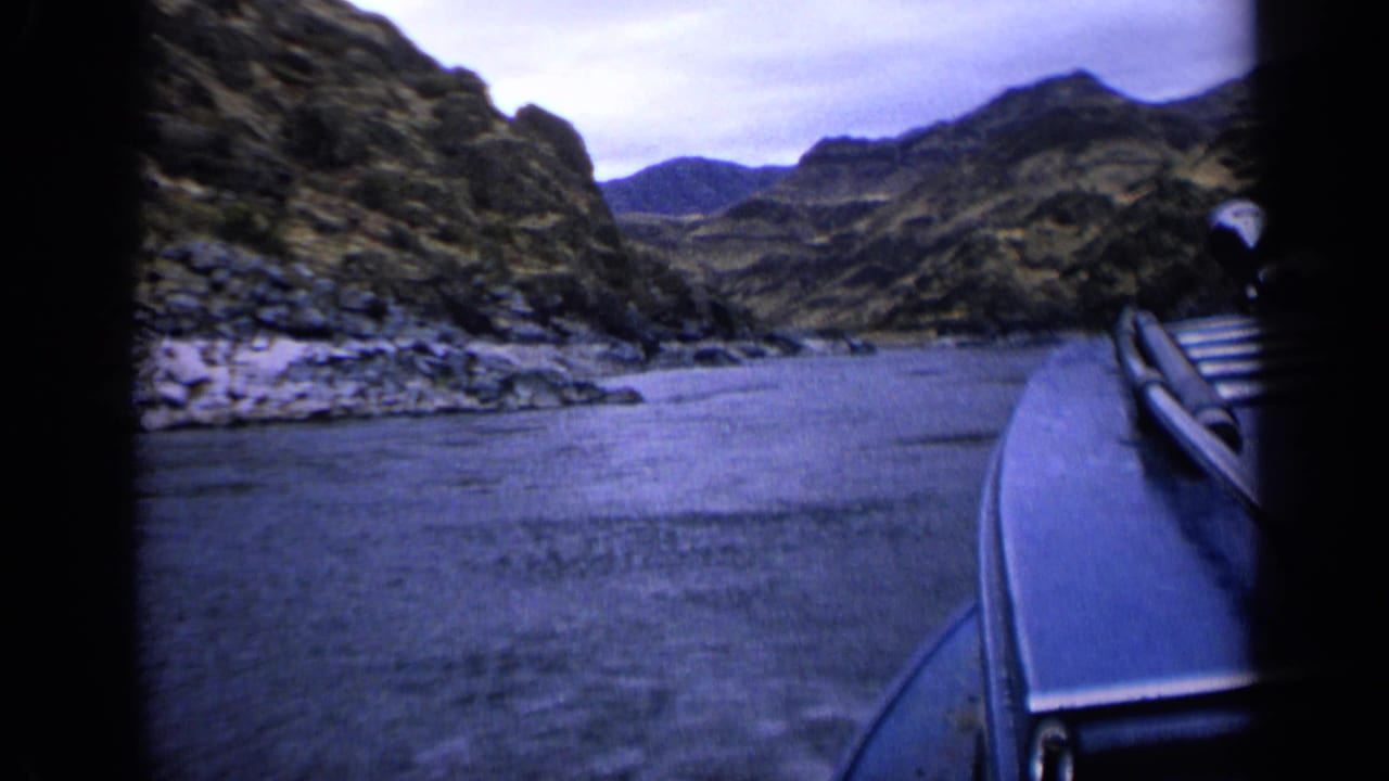 1963 Idaho 8mm frame showing a boat-side view of river water, rocky shore, and arid canyon hills.