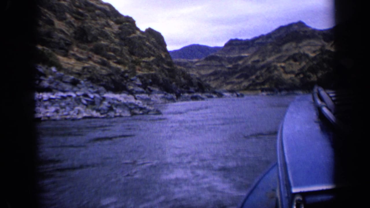 1963 Idaho 8mm frame showing the boat beside a wide river channel bordered by rugged canyon terrain.