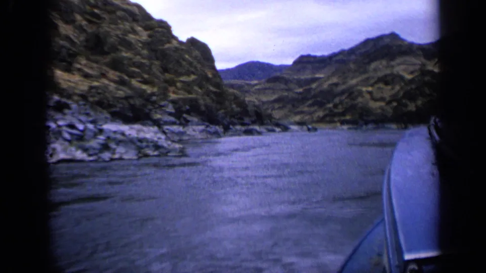 1963 Idaho 8mm frame from a boat moving through a rocky river canyon, with water ahead and dark frame edges visible.