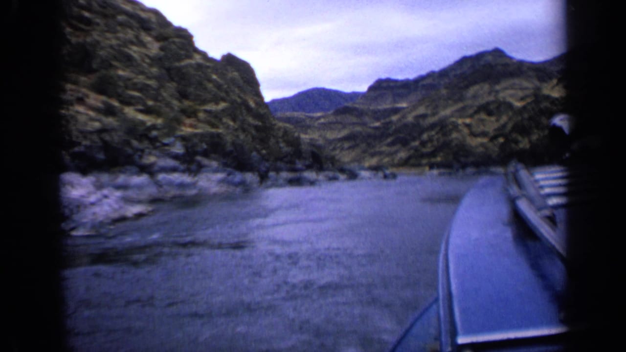 Boat bow and railing beside calm water in a rocky canyon landscape.