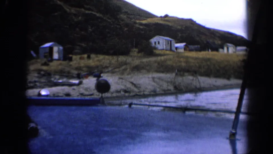 Idaho 1963 8mm frame of modest shoreline buildings and a hillside settlement seen from a moving boat.