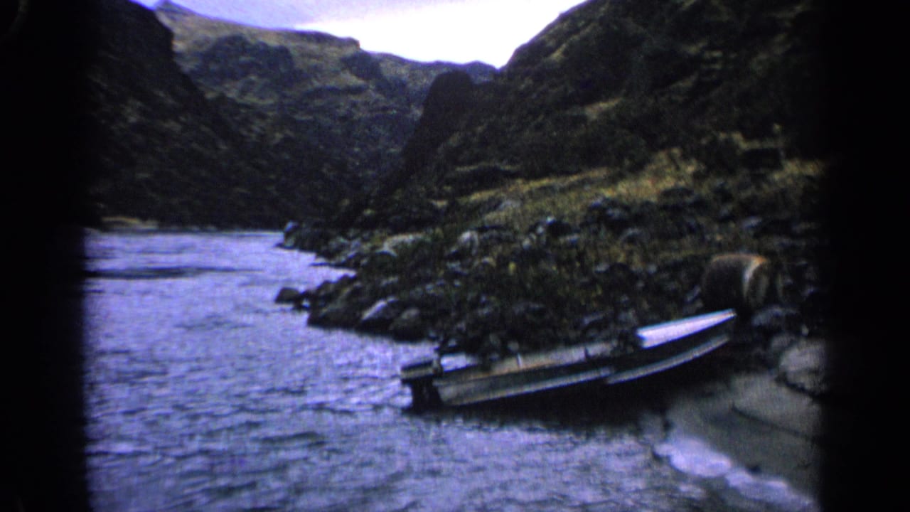 Small boat pulled onto a rocky shore beside a wide stream in a steep valley.