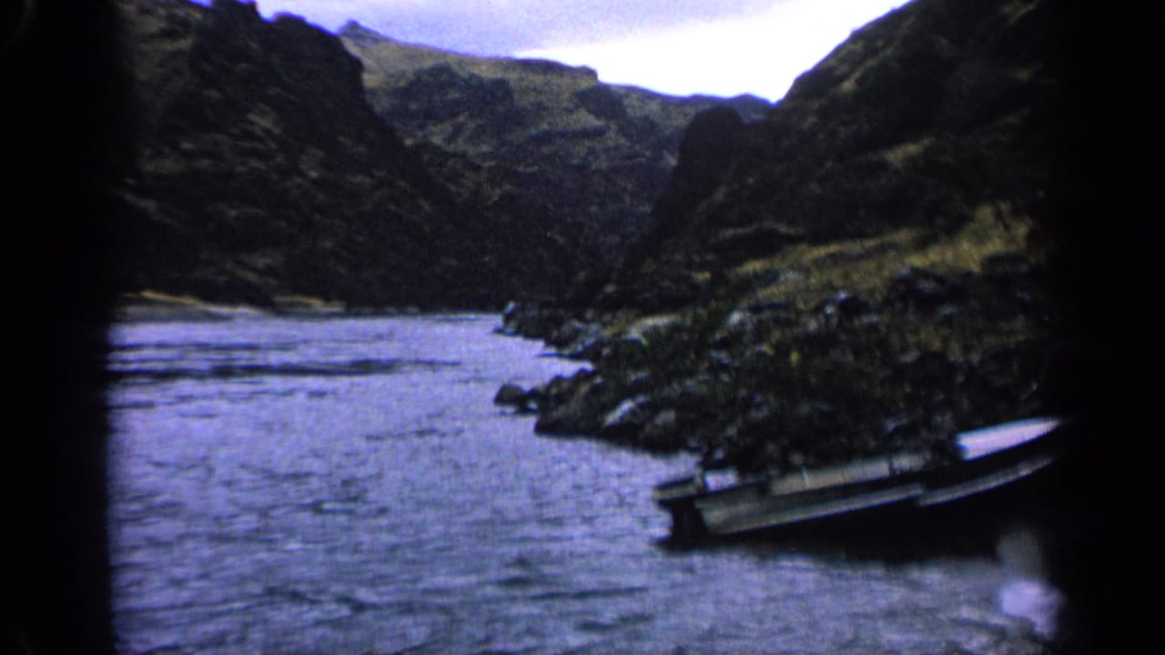 Wide stream running through a steep valley with a small boat near the right bank.