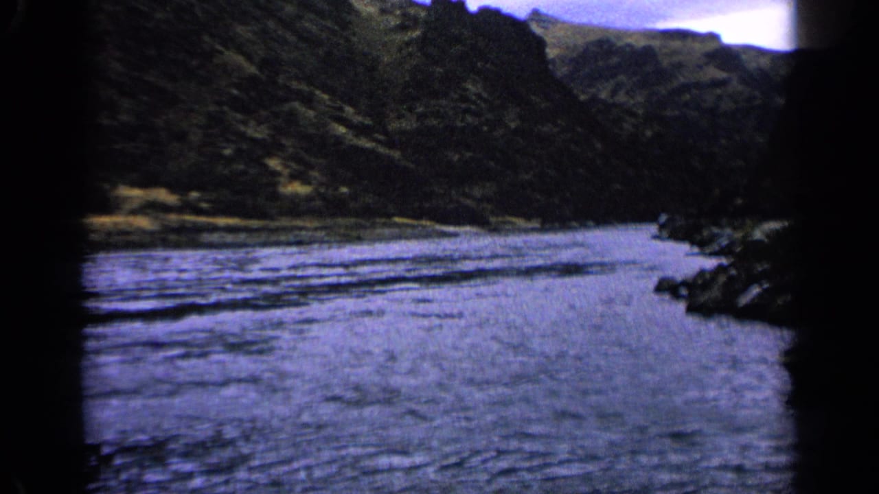 River running through a dark mountain valley under cloudy sky.