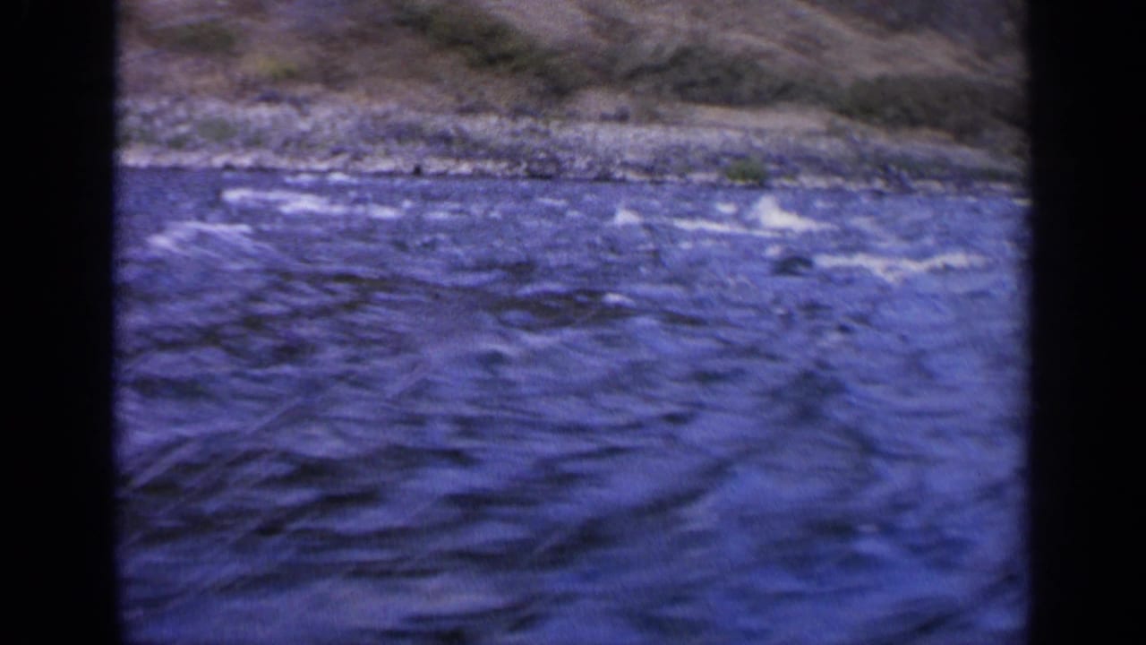 Blue river water with white ripples below a rocky bank and sloped hillside.