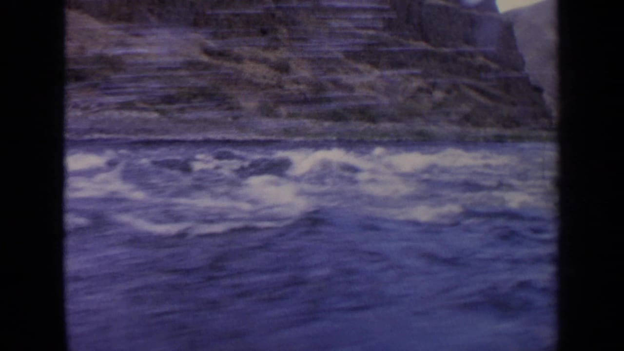Rushing blue river water beside rocky banks with black film frame edges.