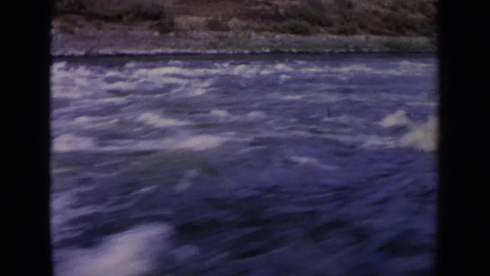 1963 Idaho 8mm frame showing foamy current, rippled blue water, a low rocky bank, and grainy home-movie color.