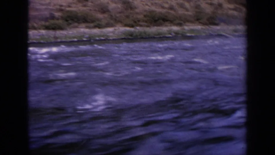 1963 Idaho home-movie frame with rippling blue water, a low shoreline, and dark vertical borders from the filming position.