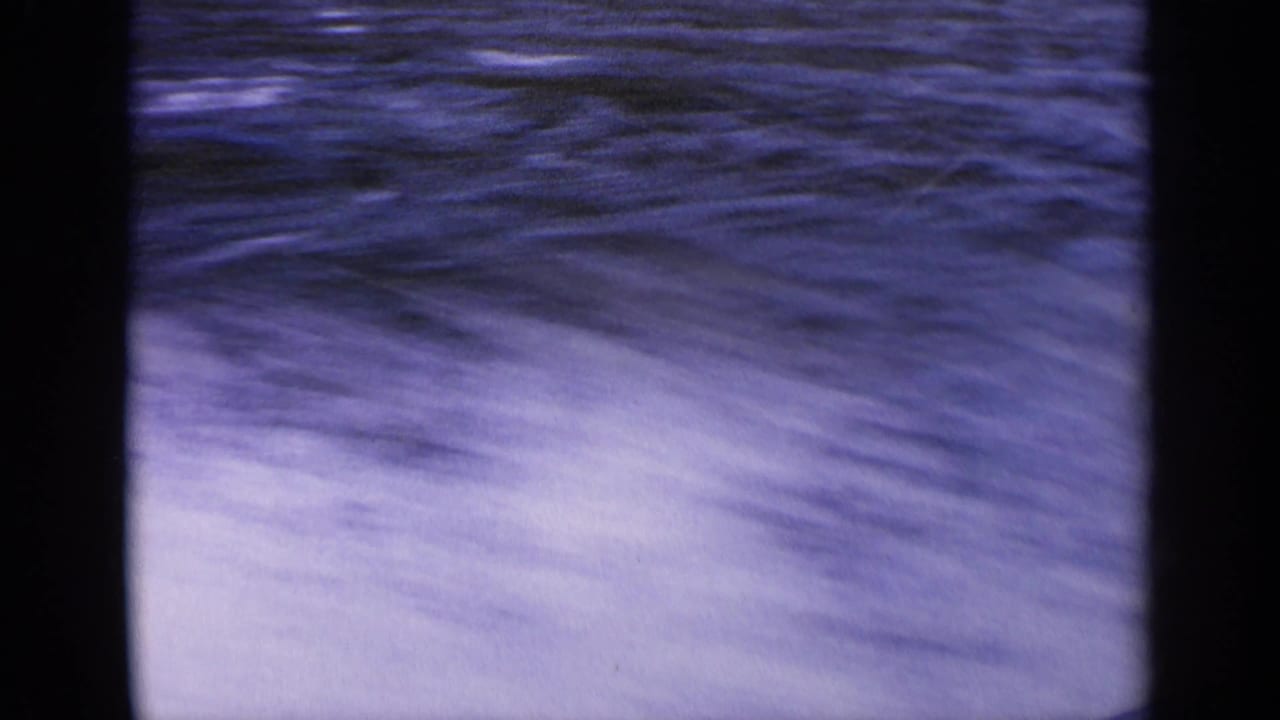Blue-purple water and white spray seen through dark film borders.