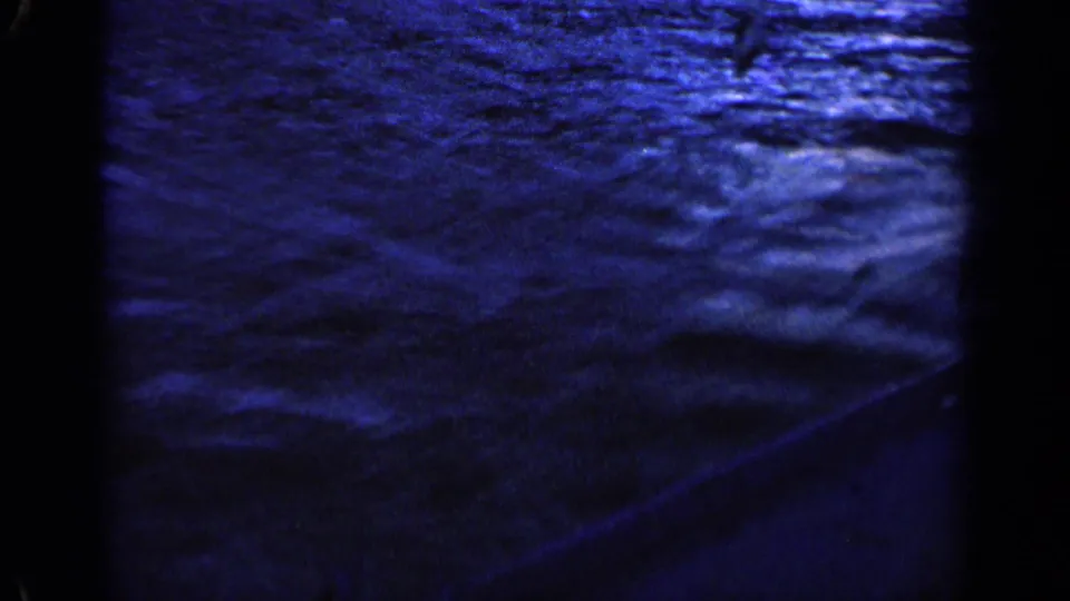 An 8mm frame shows textured blue wake and water movement beside a boat in 1963 recreational footage.