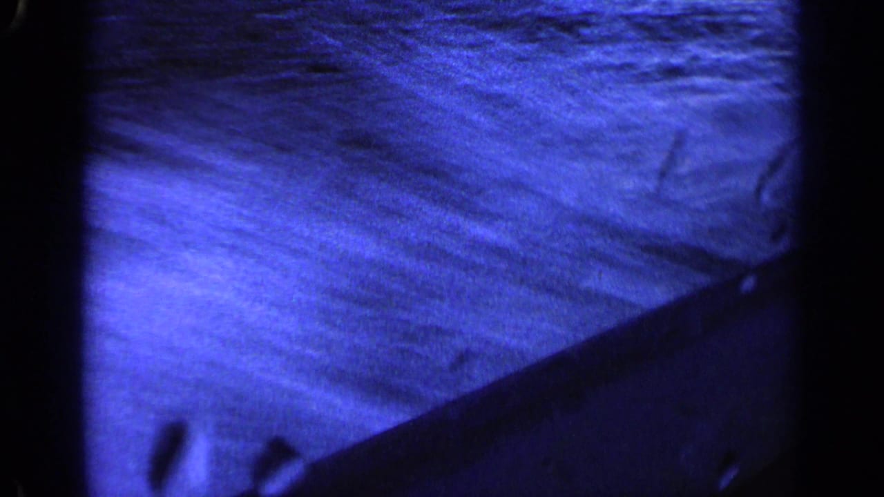 Blue-shifted 8mm frame showing rippling lake water and the dark edge of a moving boat in Idaho home-movie footage.