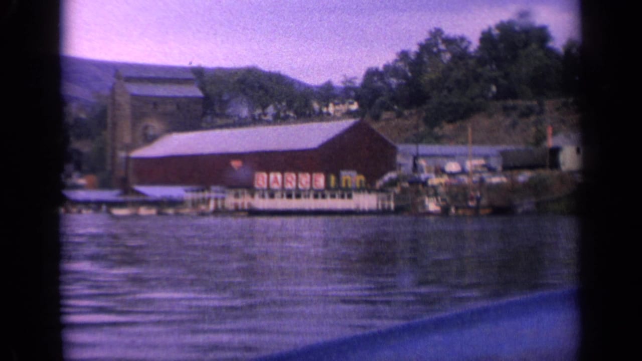 Projected 8mm view of the Idaho lakeside building and dock, with rippled lake water and tree-covered shoreline behind it.