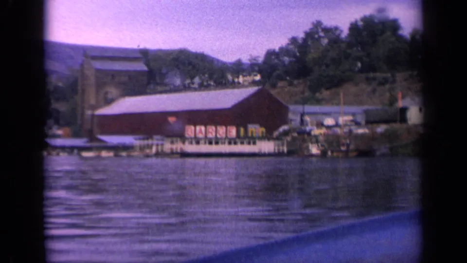 Projected 8mm view of the Idaho lakeside building and dock, with rippled lake water and tree-covered shoreline behind it.