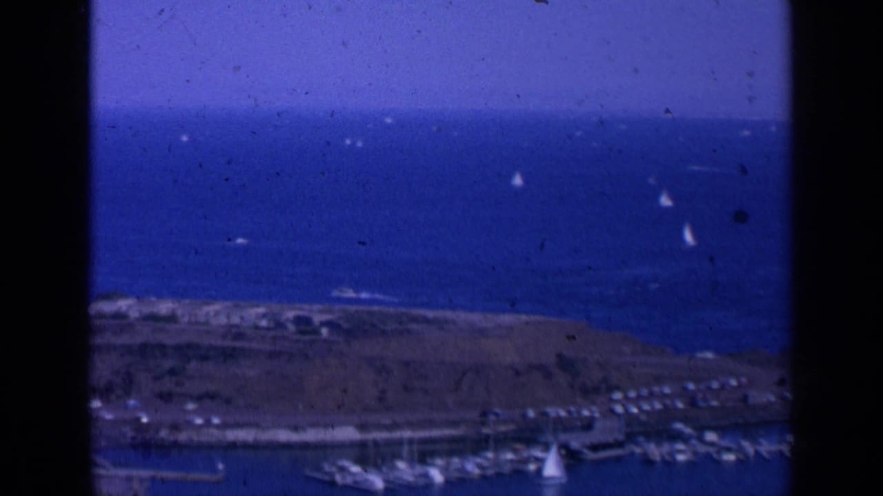 1963 San Francisco Bay home-movie frame showing blue water, small sailboats, marina docks, shoreline, and visible 8mm frame edges.