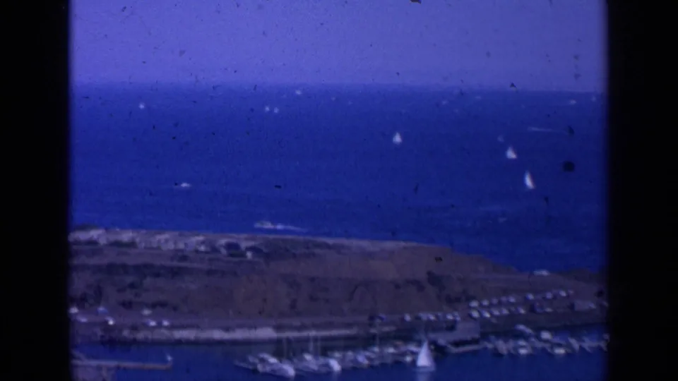 1963 San Francisco Bay home-movie frame showing blue water, small sailboats, marina docks, shoreline, and visible 8mm frame edges.