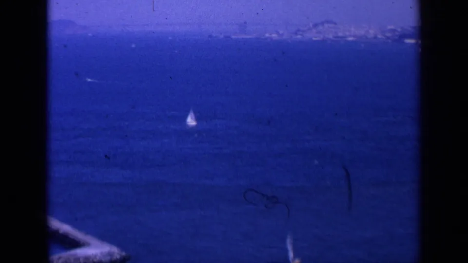 1963 San Francisco bay scene with a small sailboat on open blue water and a hazy shoreline beyond.