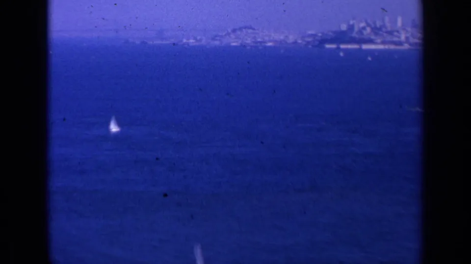 1963 San Francisco bay view with a small sailboat in the foreground and distant city skyline along the horizon.