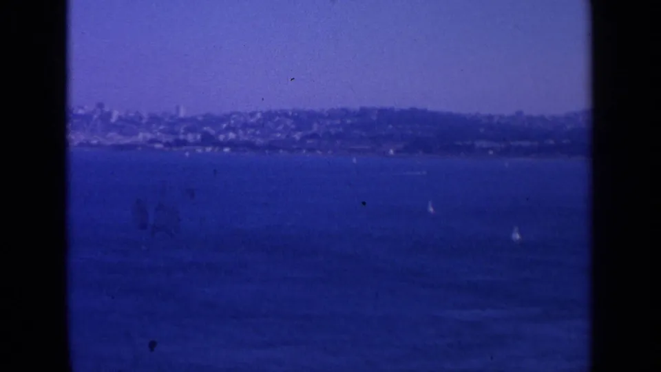 Distant San Francisco shoreline across blue water, with small white sailboats and a soft hillside skyline under clear sky.