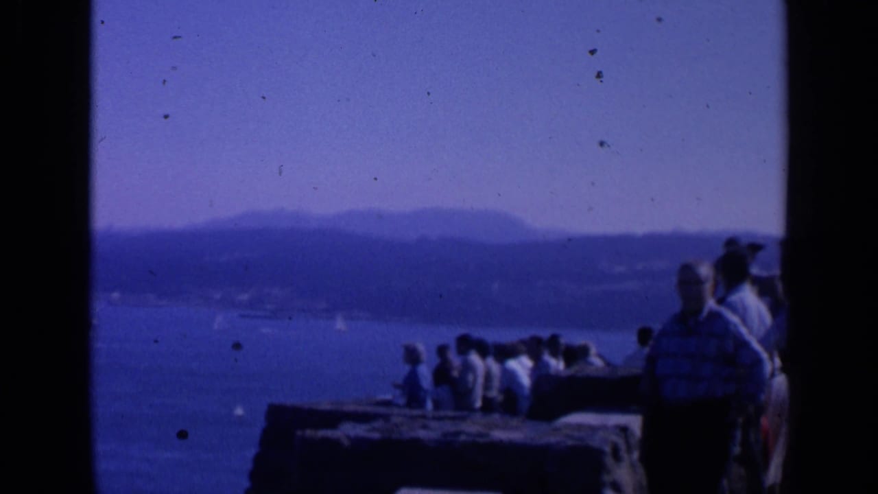 Tourists stand at a stone overlook facing San Francisco Bay and the Golden Gate Bridge.