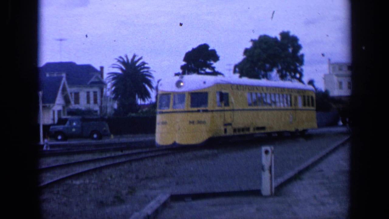Yellow railcar on tracks near houses, a palm tree, and a parked truck.