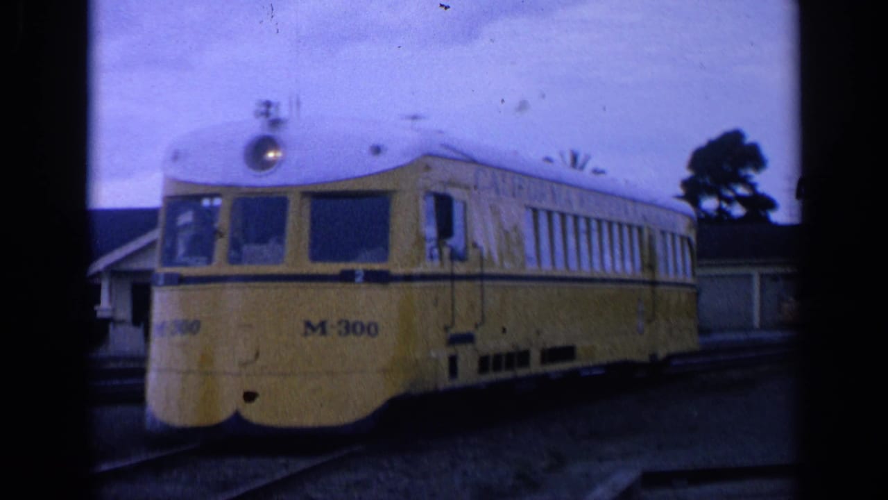 Yellow railcar on tracks beside a station area under a cloudy sky.