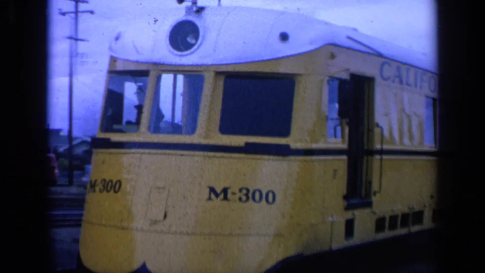 1963 San Francisco frame of the yellow M-300 streetcar on tracks, with a person visible inside near the front window.