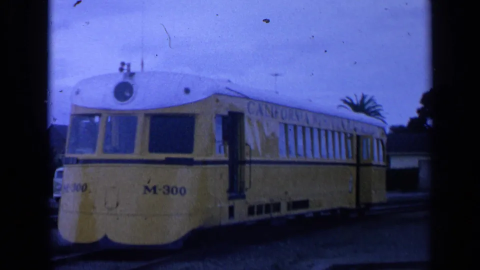 1963 San Francisco frame showing the yellow M-300 streetcar on tracks, with a palm tree, buildings, and power lines behind it.