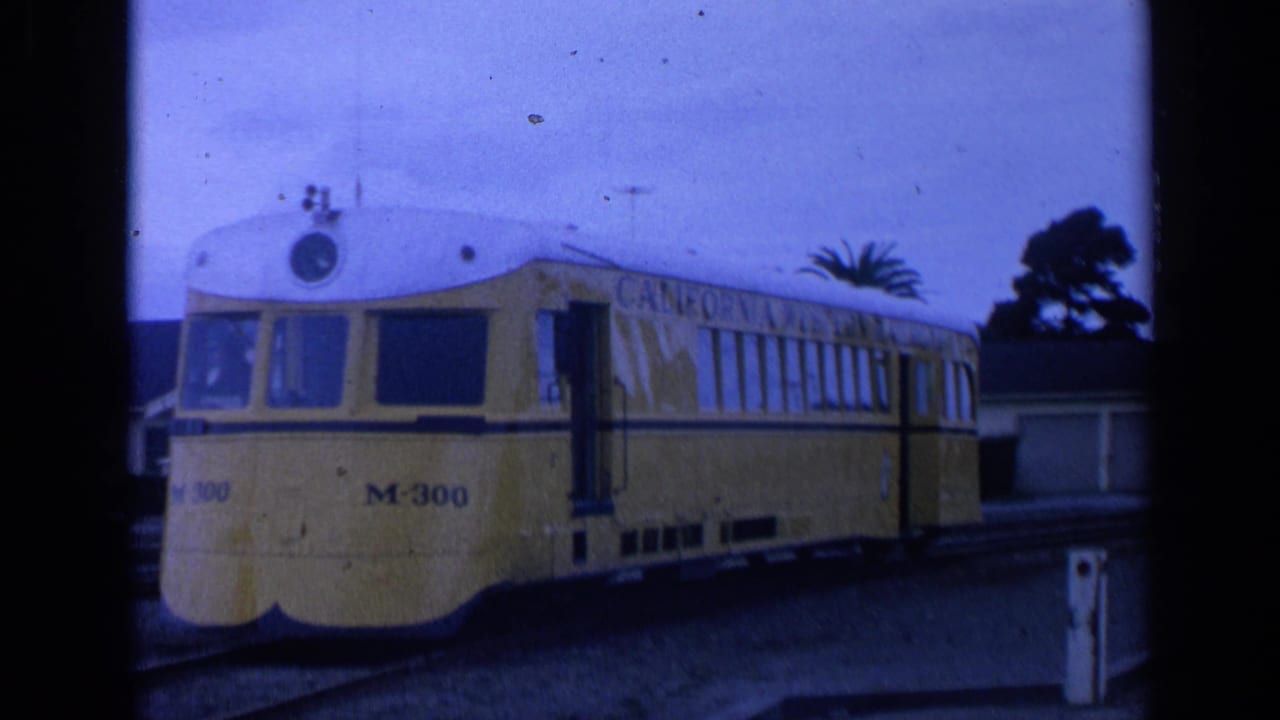Yellow railcar marked M-300 stopped on tracks near low buildings.