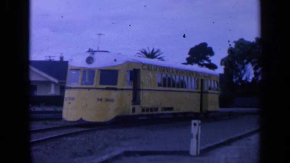 Closer 1963 view of the yellow M-300 railcar, showing its rounded front, windows, side lettering, and nearby station platform area.