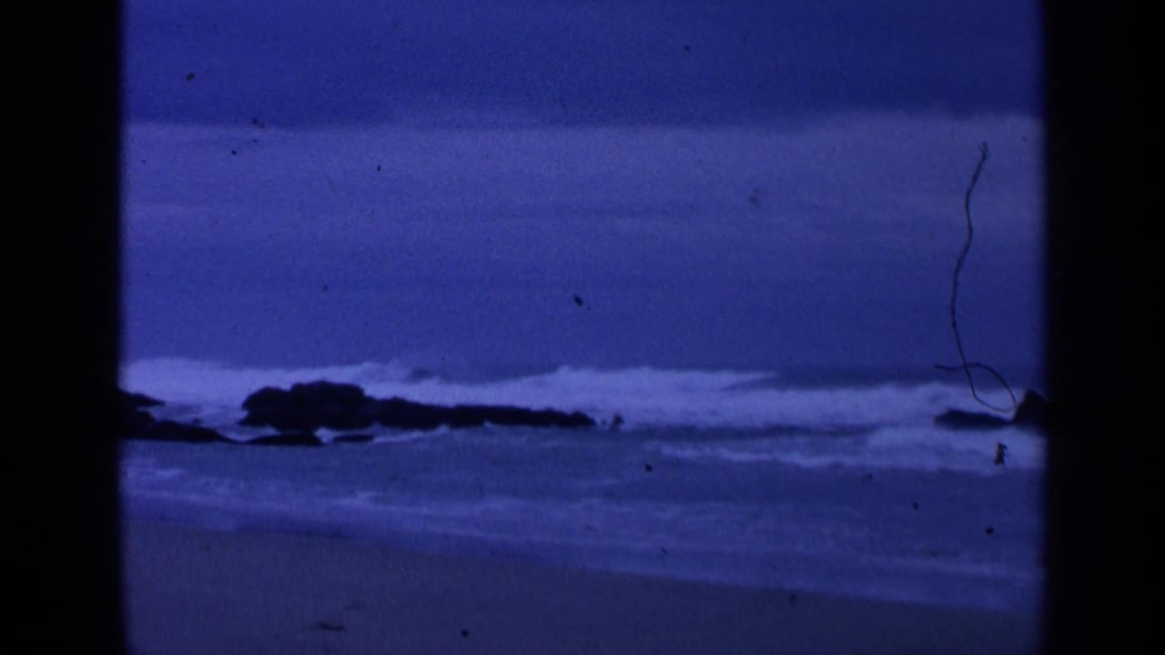 Blue-tinted shoreline with waves breaking against dark rocks.
