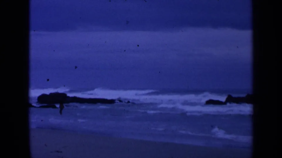 Blue-toned 8mm coastal frame with surf bands, dark rocks, and soft horizon detail near San Francisco per clip metadata.
