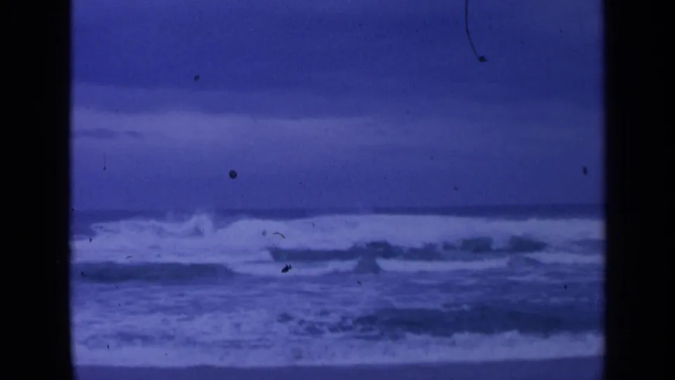 1963 San Francisco shoreline frame showing a breaking wave and blue overcast coastal horizon on 8mm film.