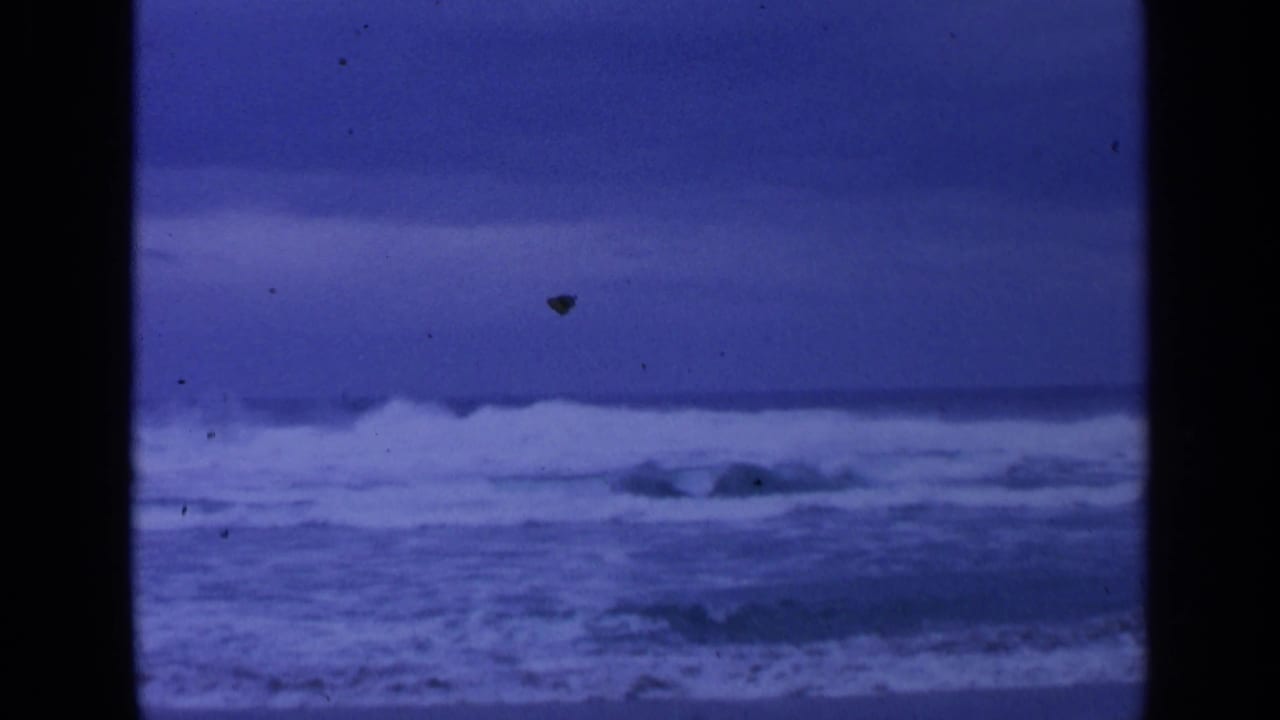 1963 8mm home-movie frame of rough ocean surf near San Francisco, with whitecaps under a deep blue-gray sky.
