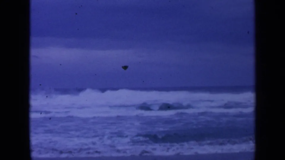 1963 8mm home-movie frame of rough ocean surf near San Francisco, with whitecaps under a deep blue-gray sky.