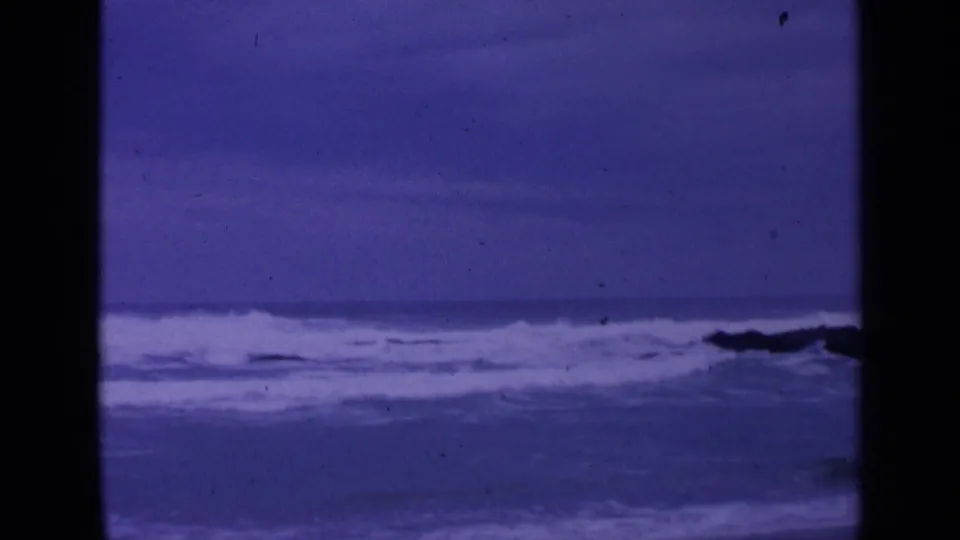Final 1963 8mm frame of rough surf near San Francisco, with white water and a dark shape that may be shoreline rocks.