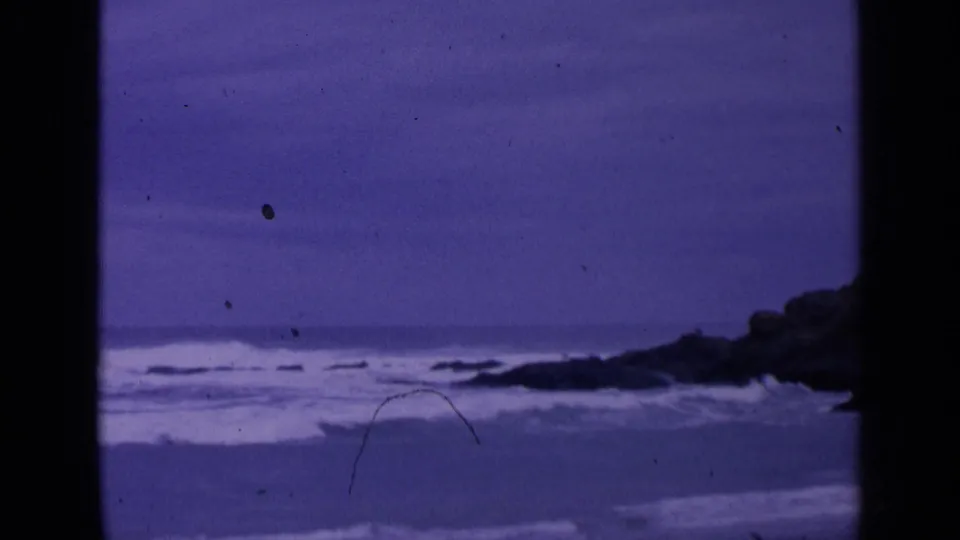 Purple-tinted 8mm coastal frame showing surf, horizon, and dark rocks near San Francisco in 1963.