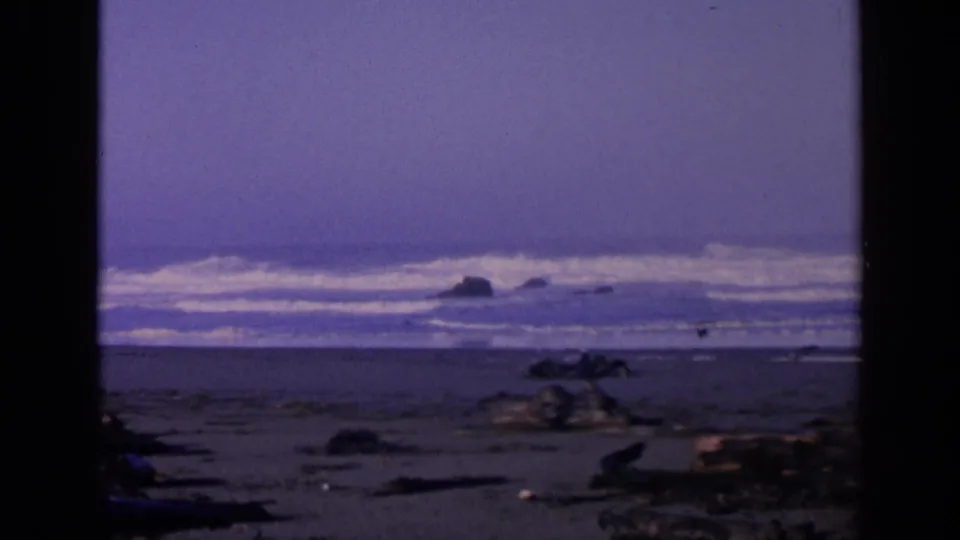 1963 San Francisco coastal frame with blue surf, beach debris, offshore rocks, and visible 8mm gate edges.