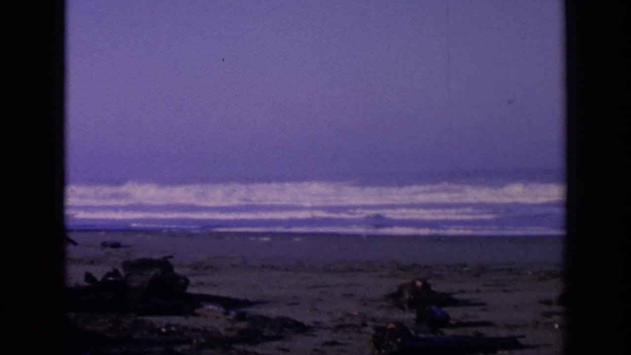 San Francisco shoreline in 1963, with white surf bands beyond a dark beach foreground of rocks and driftwood.
