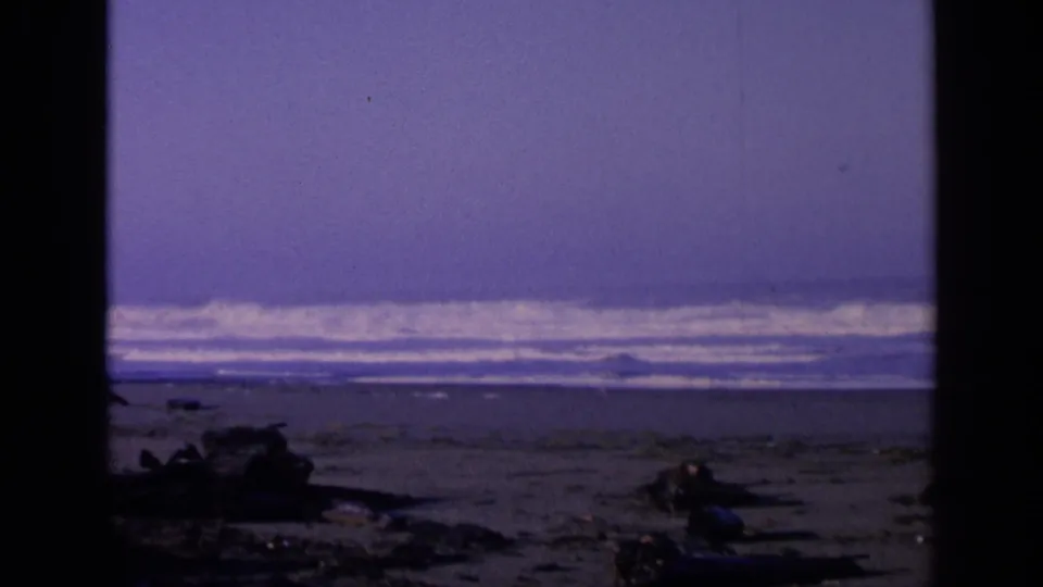 San Francisco shoreline in 1963, with white surf bands beyond a dark beach foreground of rocks and driftwood.