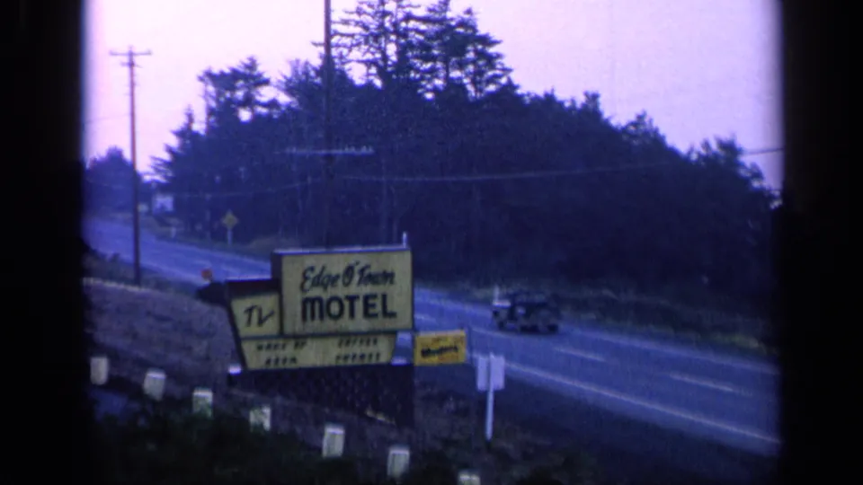 1963 roadside motel sign near San Francisco with a classic car passing under a purple-tinged sky.